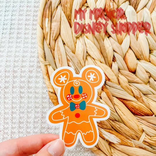 Gingerbread man-shaped sticker held by a hand on a woven mat background with 'My Magical Disney Shopper' text.